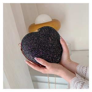 Detail of heart-shaped black sequin clutch bag with gold chain strap held in hands