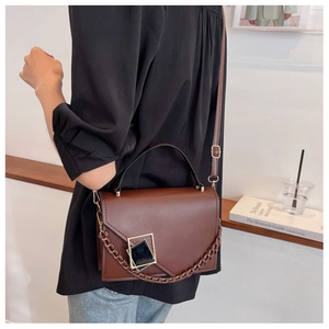 Brown leather crossbody bag with gold buckle and chain detail worn by a model