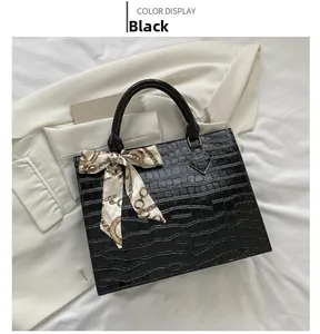 Detail of black crocodile texture handbag with chain print silk scarf on top handle
