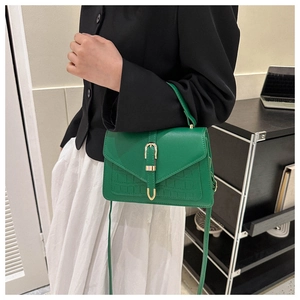 Close-up of dark green crossbody bag with crocodile embossing and golden U-shaped buckle