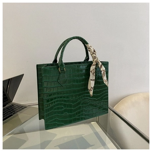 Detail of dark green croc-embossed tote bag with decorative silk scarf on handle