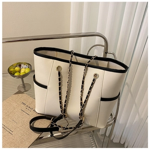 Detail of cream tote bag featuring black contrast trim and metal chain leather straps