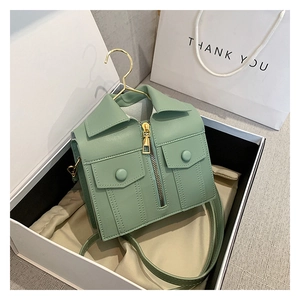 Detail view of a mint green jacket-shaped handbag with metal zippers in a gift box