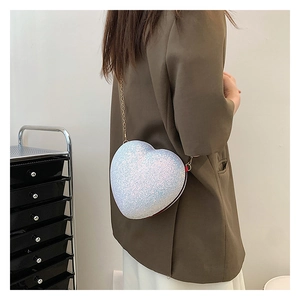 Detail of white glitter heart crossbody bag with gold chain strap worn by a model