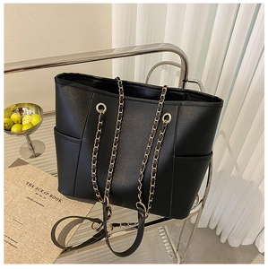 Detail of black tote bag with lychee texture, gold chain strap and side pockets