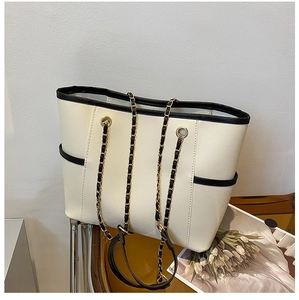 Detail of cream tote bag featuring black trim and gold chain woven shoulder strap