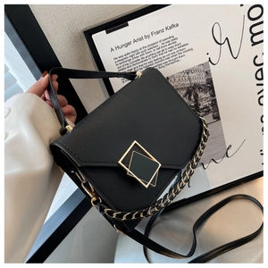 Detail of a black leather crossbody bag featuring a designer geometric gold buckle and chain