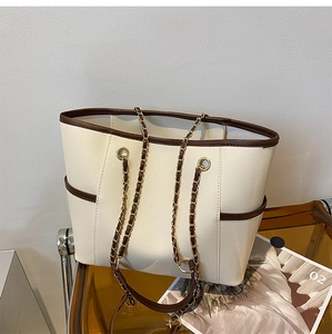 Detail of cream tote bag with brown trim, side pockets and gold chain leather strap