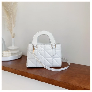 Detail of white quilted handbag with gold hardware and wide handle on wooden shelf