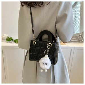 Detail of black mini crossbody bag with triangular quilting and fuzzy monster charm
