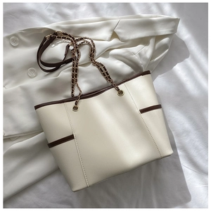 Chic cream tote bag with brown trim and gold chain strap on a white blazer background
