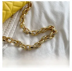 Detail of yellow quilted faux leather bag featuring thick gold acrylic chain strap