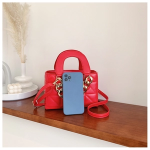 Close-up of red quilted mini handbag with gold chain detail and phone for size reference
