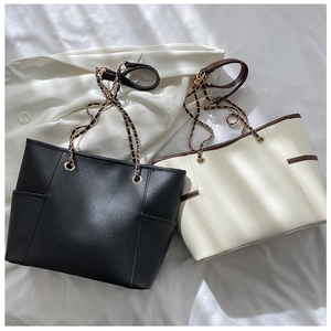 Detail of minimalist leather tote bag featuring side pockets and metal chain straps