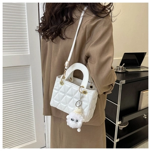 Detail of white quilted crossbody bag with golden ring buckle and plush keychain