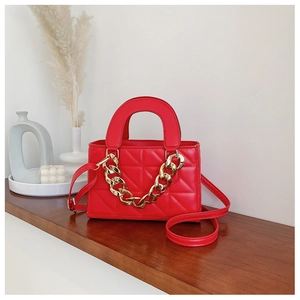 Red quilted handbag with gold chain detail on wooden shelf with minimalist decor