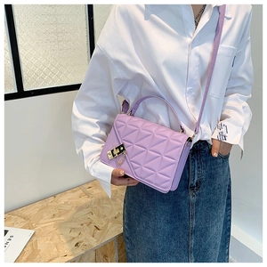 Detail of light purple quilted crossbody bag with metal lock and chain strap on a model