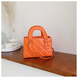 Detail of bright orange quilted handbag with golden hardware on a wooden shelf