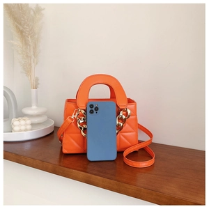 Detailed view of orange quilted PU leather handbag with chunky gold chain and smartphone