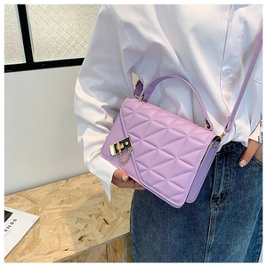 Detail of purple quilted shoulder bag with gold square clasp worn by model in casual style