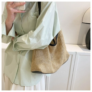 Detail of woven straw tote bag featuring black leather trim and mesh texture on a model