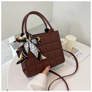 Détail du sac bandoulière marron foncé matelassé avec foulard à pois sur la poignée