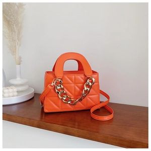 Orange quilted handbag with chunky gold chain detail on a minimalist wooden display