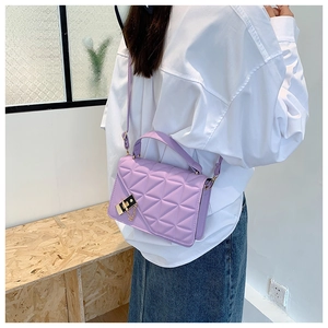 Detail of a purple quilted crossbody bag with gold twist lock on a white shirt background