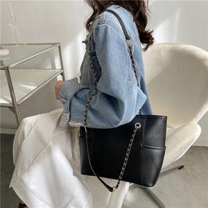 Classic black leather tote bag with metal chain strap worn by a model in casual setting