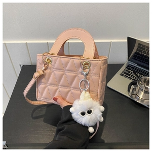 Detailed view of pink quilted handbag featuring a white plush monster pendant and gold hardware