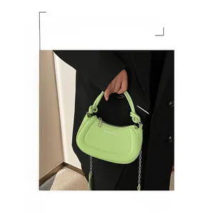 Close-up of a light green half-moon bag with a knotted handle and silver chain strap