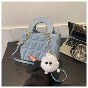 Detail of light blue quilted leather handbag with plush charm in office setting