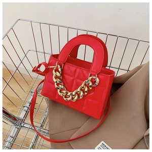 Detail of red quilted faux leather handbag with matte gold chunky chain in metal basket