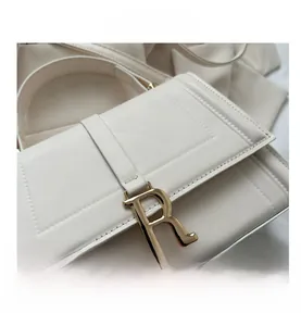 Detailed view of the gold R letter metal clasp and stitching on white leather handbag
