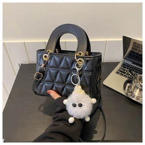 Macro shot of black quilted faux leather handbag with circular handle and plush charm