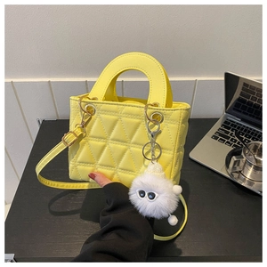 Detail of bright yellow quilted handbag with plush charm and detachable shoulder strap