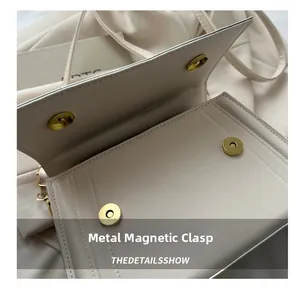 Detail view of the secure magnetic snap closure in gold on a beige leather crossbody bag