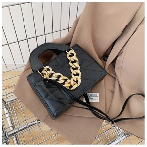 Detail of black quilted handbag with chunky gold chain on a tan blazer