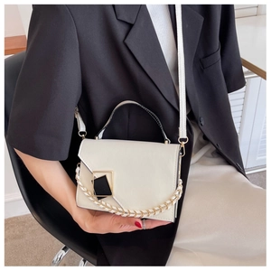 Minimalist ivory crossbody bag featuring a geometric gold buckle and woven chain strap