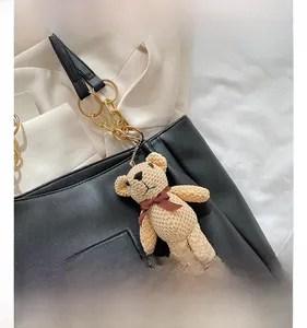 Close-up of a cute beige knitted bear pendant with dark brown bow on a black PU handbag