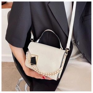 Detail of cream crossbody bag featuring a black geometric clasp and woven chain decoration