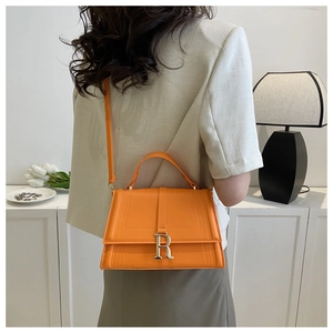 Detail of a bright orange leather bag with silver R-logo buckle shown on a model's shoulder