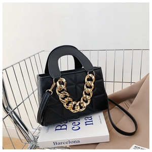 Close-up of black quilted handbag with chunky gold chain detail on a white book