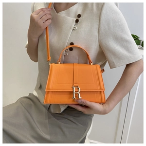 Close-up of bright orange crossbody bag featuring a gold R-letter buckle and smooth leather