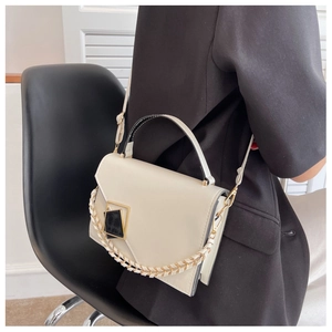 Chic beige crossbody bag with decorative metal chain shown on model in black blazer