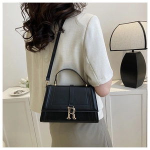 Chic black handbag with gold R buckle shown being worn by a model in a minimalist setting