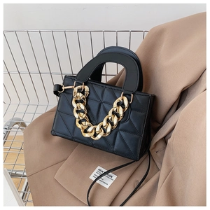 Detail of black quilted handbag with chunky gold chain on a tan blazer jacket