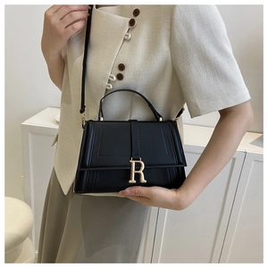Detail of minimalist black crossbody bag with gold R-buckle and elegant top handle