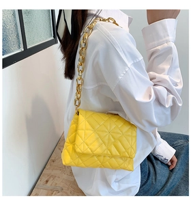 Detail view of bright yellow quilted shoulder bag with bold gold acrylic chain strap