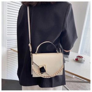 Close-up of beige leather crossbody bag with geometric metal buckle and chain handle